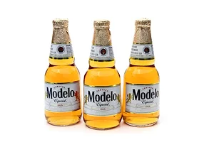 THREE BOTTLES OF MODELO BEER STAND IN A ROW ON A WHITE BACKGROUND