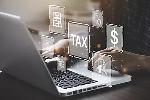 A PAIR OF HANDS WORKS AT A LAPTOP, SURROUNDED BY FINANCIAL SYMBOLS