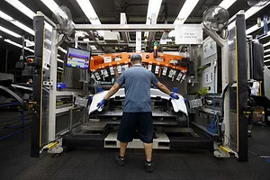 A WORKER PLACES A METAL PART ON AN AUTOMOBILE DURING MANUFACTURING