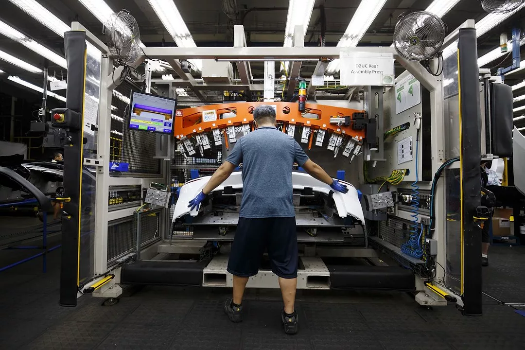 A WORKER PLACES A METAL PART ON AN AUTOMOBILE DURING MANUFACTURING