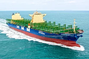 A blue and red striped container ship with "HMM" written along the side in large white lettering, with a green deck and two yellow towers