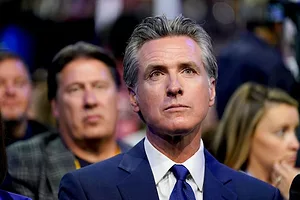 A MAN WITH SALT AND PEPPER HAIR IN A BLUE SUIT AND BLUE TIE LOOKS OFF INTO THE DISTANCE IN A CROWD