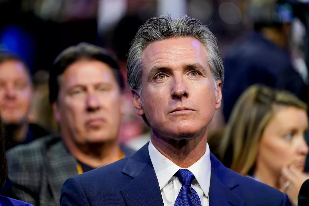 A MAN WITH SALT AND PEPPER HAIR IN A BLUE SUIT AND BLUE TIE LOOKS OFF INTO THE DISTANCE IN A CROWD