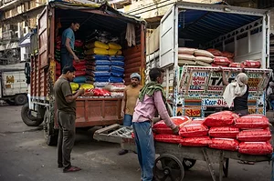 A GROUP OF MEN AND WOMEN UNLOAD SACKS OF FOOD FROM THE BACK OF A TRUCK
