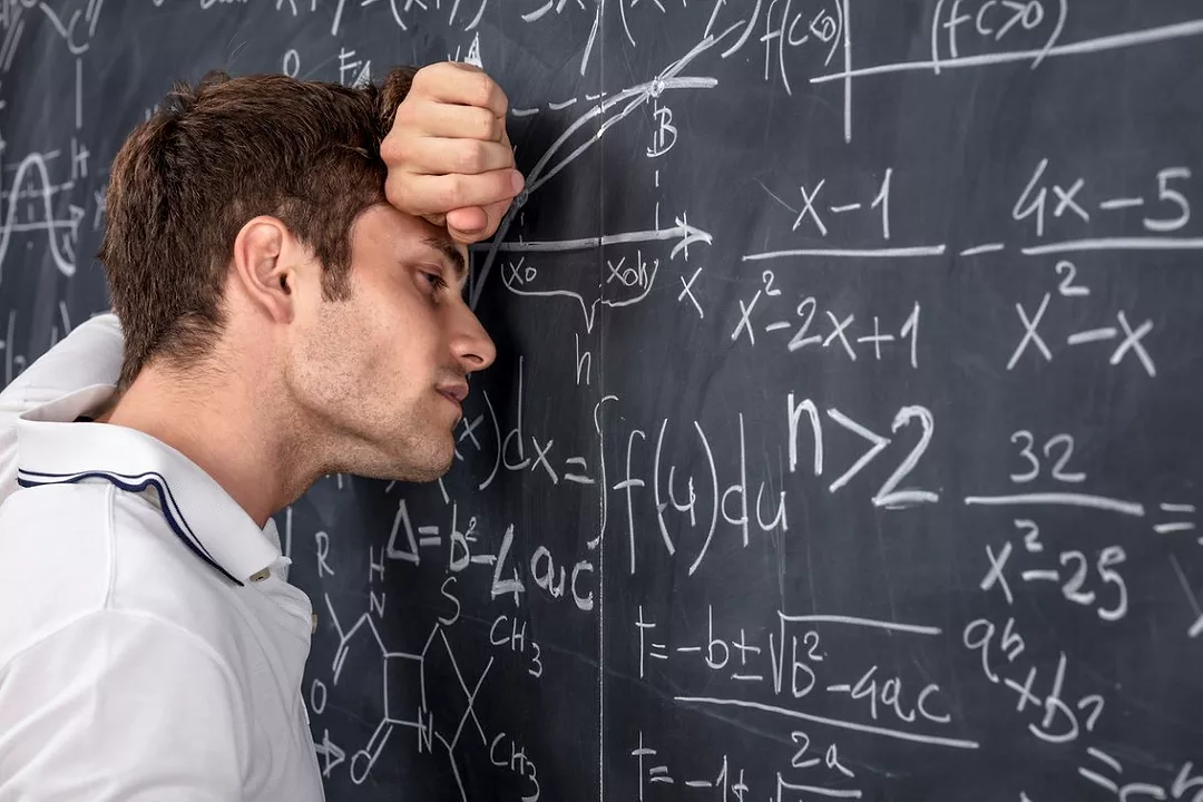 A MAN LEANS WITH HIS EYES CLOSED IN DESPAIR ON A BLACKBOARD FULL OF MATHEMATICAL EQUATIONS