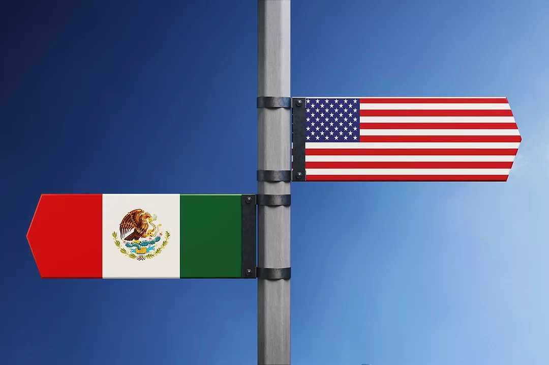 A SIGNPOST SHOWS TWO FLAGS POINTING IN OPPOSITE DIRECTIONS, US AND MEXICO