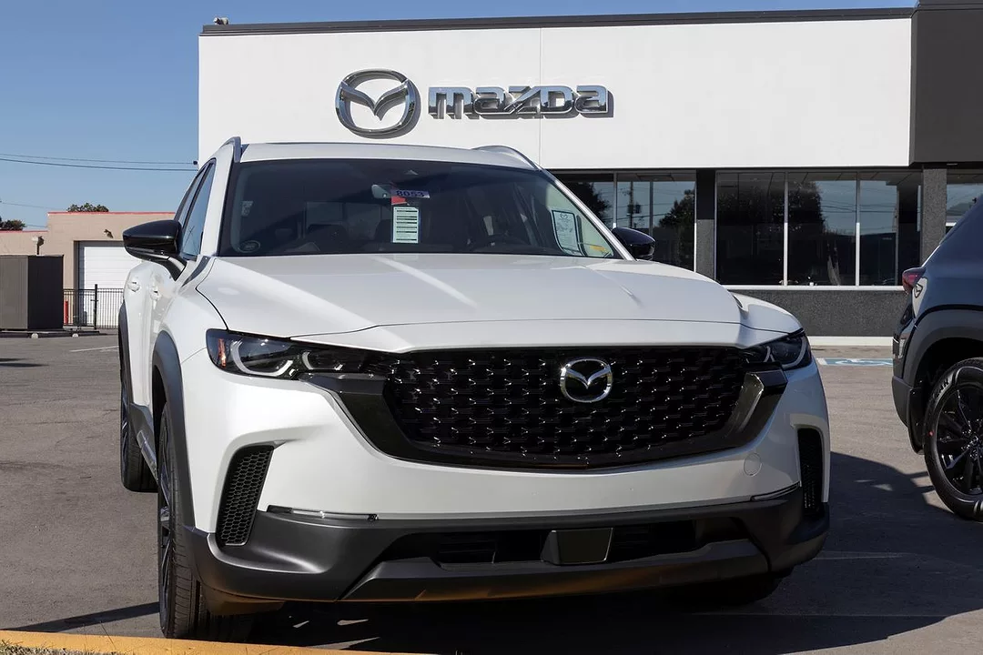 A WHITE SUV SITS PARKED IN FRONT OF A MAZDA DEALERSHIP