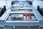 The grey, silver chassis of an unfinished electric vehicle sitting in a white, sterile room