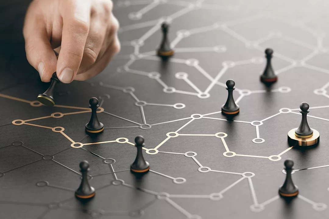 A HAND MOVES CHESS PAWN PIECES AROUND A SERIES OF INTERCONNECTED BRIGHT LINES ON A MATT SURFACE