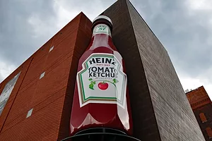 A giant red Heinz ketchup bottle positioned at the corner of a tall red brick building