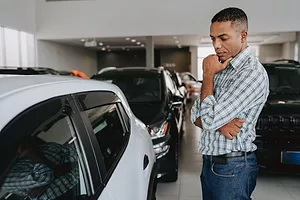A MAN STROKES HIS CHIN WHILE LOOKING AT AN AUTOMOBILE IN A CAR DEALERSHIPdreswd-1913373628.jpg