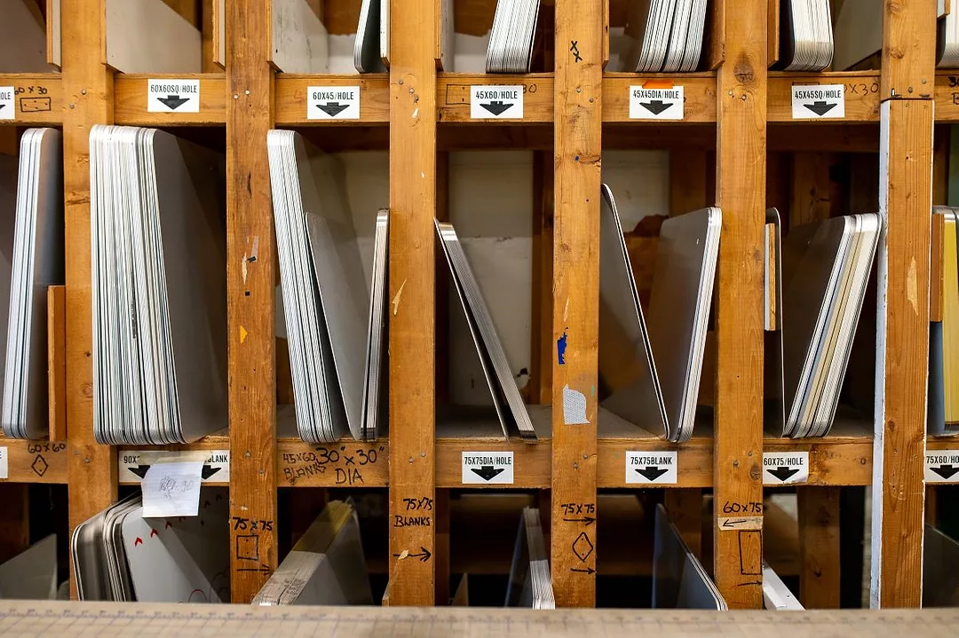 MULTIPLE SHEETS OF METAL SIT STACKED IN WOODEN CUBBY HOLES