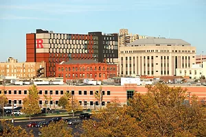 A collection of red brick and white buildings along a skyline with a red "R" on the outside of one