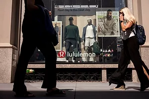 PEDESTRIANS SEEN FROM THE WAIST DOWN PASS BY A BRIGHTLY LIT STORE FRONT BEARING THE LULULEMON LOGO