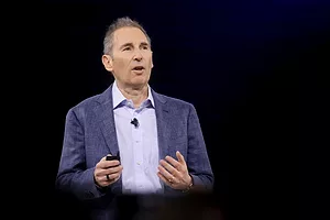 A MAN IN A JACKET AND SHIRT, WEARING A LANIER MIC, HOLDS HIS HANDS OUT AS HE SPEAKS