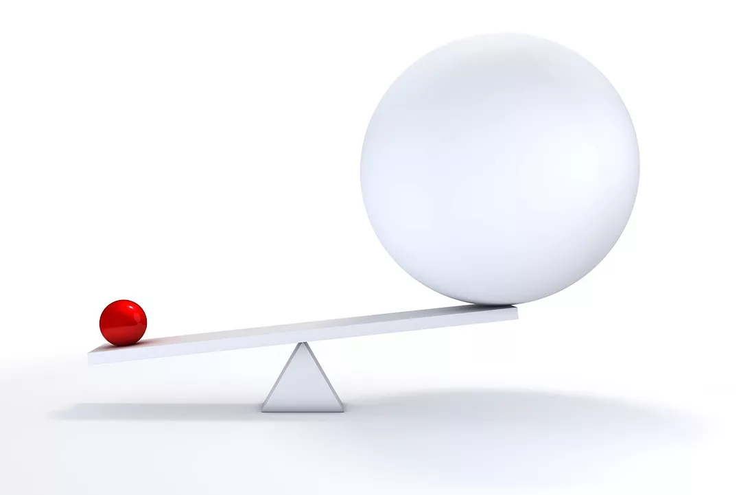 A TEETER-TOTTER HOLDS A LARGE WHITE BALL, OUTBALANCED BY A SMALL RED BALL