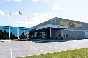 A LOW-SLUNG OFFICE BUILDING AND PARKING LOT, WITH DHL FLAGS VISIBLE