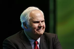An elderly man with white hair wearing a black sport coat and red tie