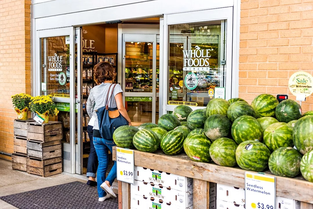 A SHOPPER WALKS PAST A PILE OF WATERMELONS ON HER WAY INTO A WHOLE FOODS STORE FRONT