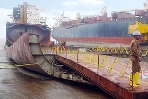 A WORKER IN A HARDHAT STANDS ON THE DOCK NEAR A PARTIALLY DECONSTRUCTED SHIP