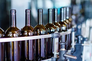 A row of dark wine bottles on a metallic conveyer belt