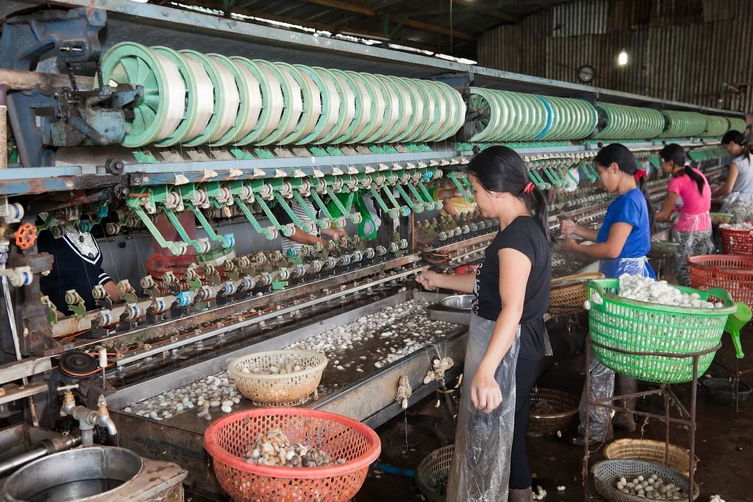TWO WOMEN STAND IN FRONT OF GIANT LOOM MACHINES