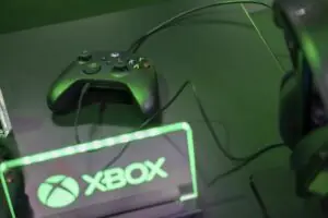 A GAMING CONTROL CONSOLE SITS BEHIND A LIGHTED SIGN SAYING XBOX