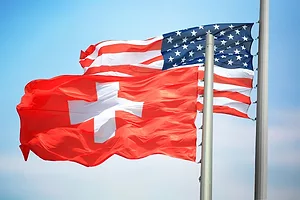 THE FLAGS OF SWITZERLAND AND THE US FLUTTER TOGETHER AGAINST A BLUE SKY