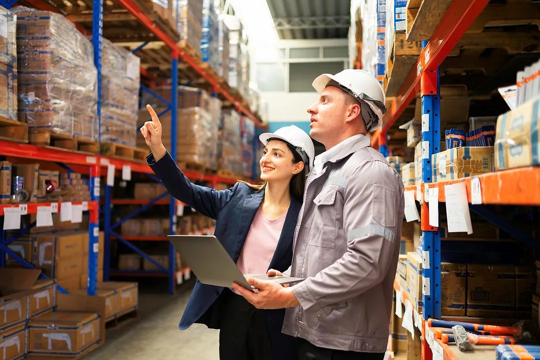 TWO WORKERS DISCUSS IN A WAREHOUSE AISLE