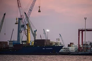 A SHIP RESTS AT DOCK UNDER A CRANE IN EARLY EVENING LIGHT