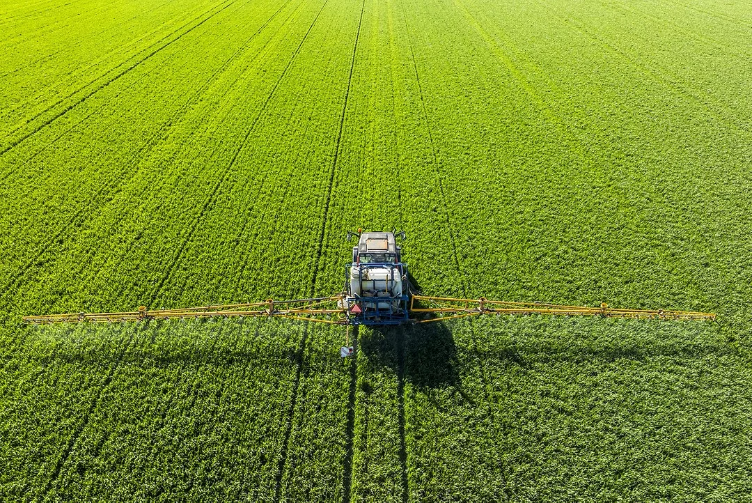A TRACTOR SPRAYS CROPS IN A GREEN FIELD, SEEN FROM ABOVE