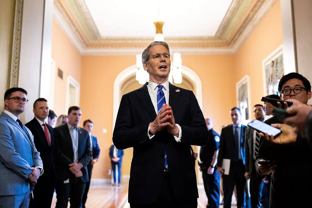 A MAN IN A SUIT AND TIE HOLDS HIS HANDS IN A GESTURE OF GREETING IN A HALLWAY OF OTHER MEN IN SUITS