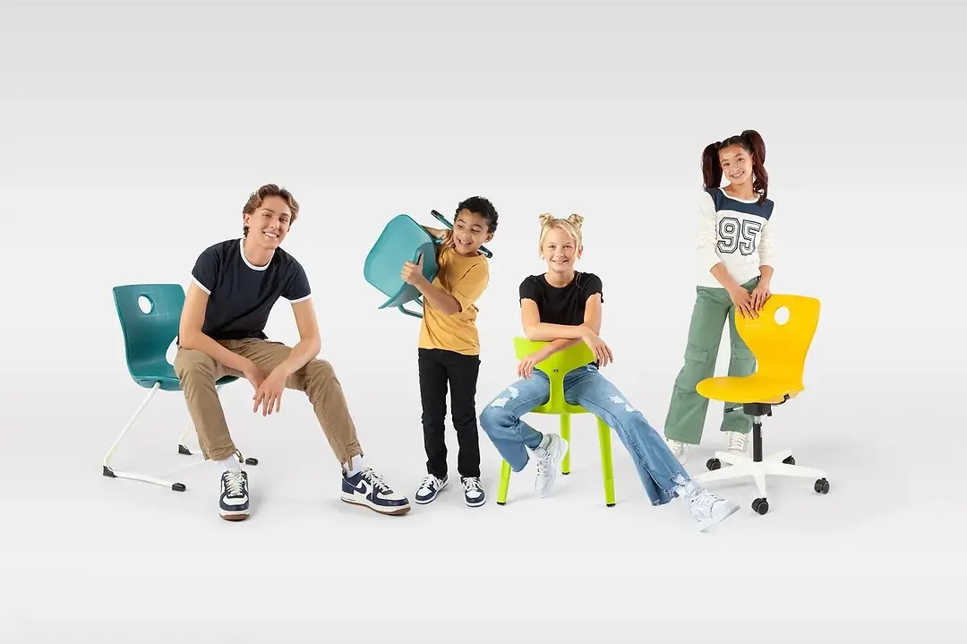 FOUR KIDS OF DIFFERENT AGES SIT ON AND PLAY WITH BRIGHTLY COLORED PLASTIC CHAIRS