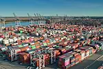 Port-of-Savannah-Georgia-iStock-1363320297.jpg Stacks of multi-colored shipping containers arranged in rows at a port, with rows of blue and grey shipping cranes lining the background along the coastline