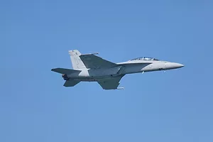 A GREY FIGHTER JET STREAKS ACROSS A CLEAR BLUE SKY