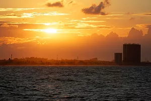 AN INDUSTRIAL PORT, SEEN FROM THE SEA, IS BATHED IN SUNSET LIGHT