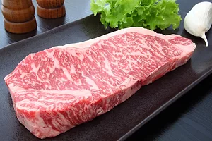 AN INTRICATELY MARBLED RAW BEEF STEAK SITS ON A BLACK CURVED PLATE
