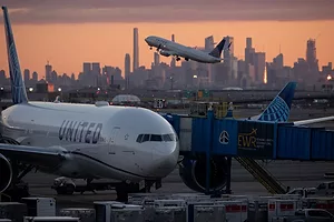 A UNITED AIRLINES PLANE SITS ON THE TARMAC, FRAMED BY A CITY SKYLINE AT SUNSET