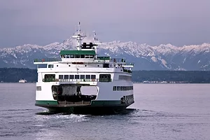 A white and green ferry boat on the water, with a snowcapped mountain range across the horizon