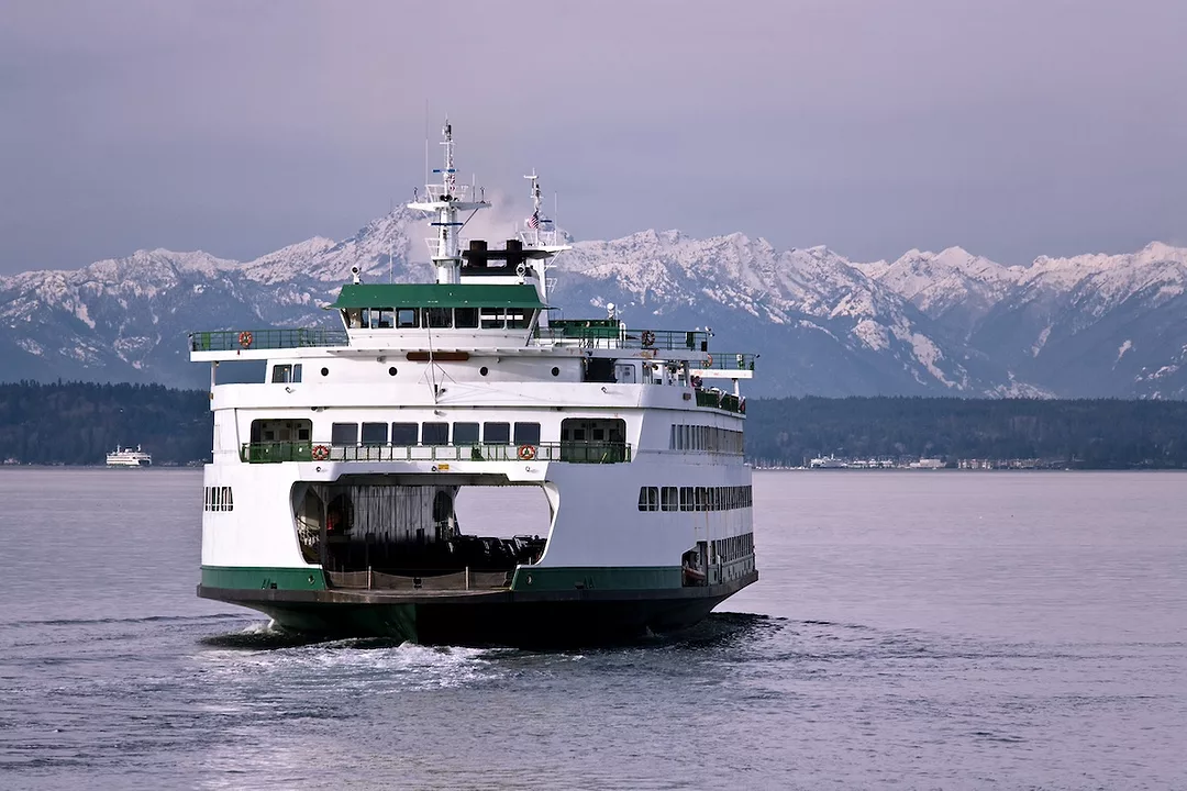 A white and green ferry boat on the water, with a snowcapped mountain range across the horizon