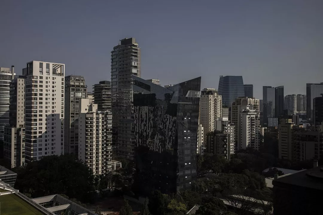 A MODERN CITY SKYLINE FULL OF TOWER BLOCKS SITS IN HEAVY SHADOWS CAST BY THE SUN
