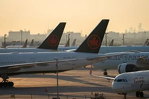 MULTIPLE AIRPLANE TAILS BEAR THE AIR CANADA INSIGNIA ON THE TARMAC OF AN AIRPORT