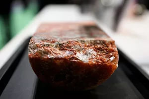 A rectangular slab of red mineral on a black surface