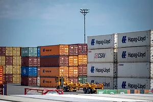 A FLATBED TRUCK DRIVES PAST STACKS OF SHIPPING CONTAINERS