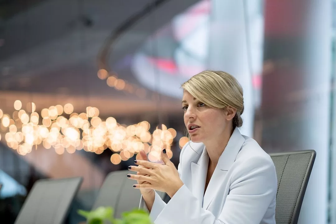 A WOMAN IN A WHITE SUIT SITS FRAMED BY OUT OF FOCUS LIGHTS