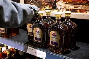 Five bottles of whisky with gold caps and labels that read "Crown Royal" in cursive lettering, sitting on a metal liquor store shelf.