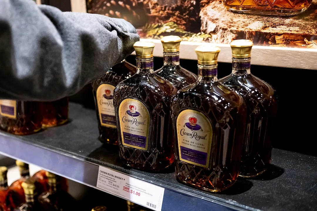 Five bottles of whisky with gold caps and labels that read "Crown Royal" in cursive lettering, sitting on a metal liquor store shelf.