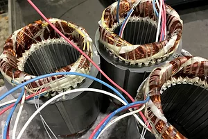 Three circular bunches of copper wiring wrapped around the top of three identical grey metal cylinders, with red, white and blue wires protruding from each