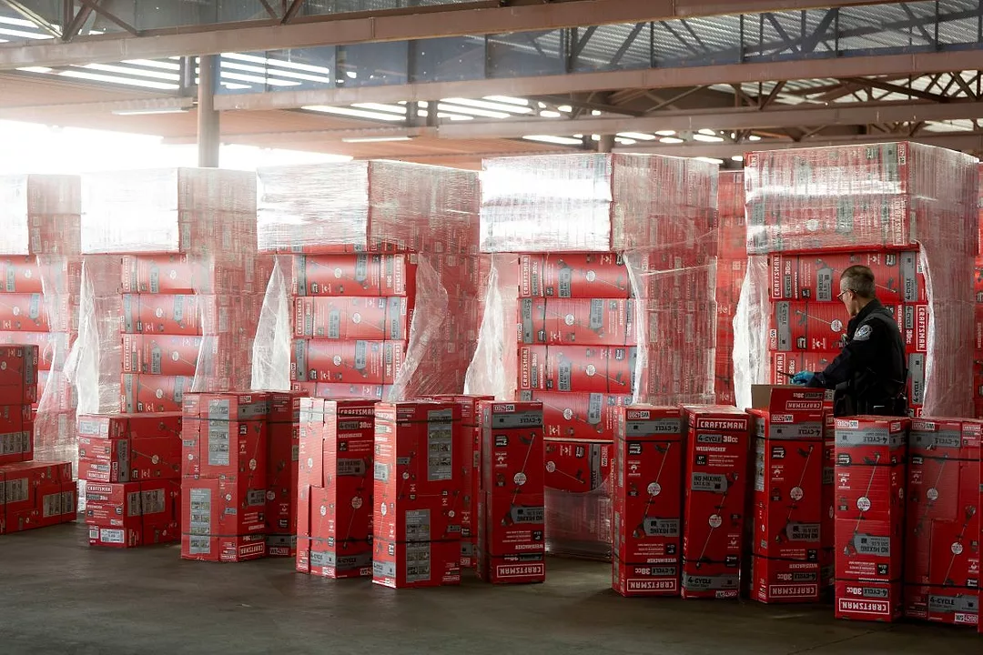 A UNIFORMED OFFICER WITH A CLIPBOARD INSPECTS STACKS OF CARGO ON PALLETS