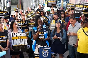 A CROWD OF PROTESTORS BEARS SIGNS READING AMAZON IS UNFAIR
